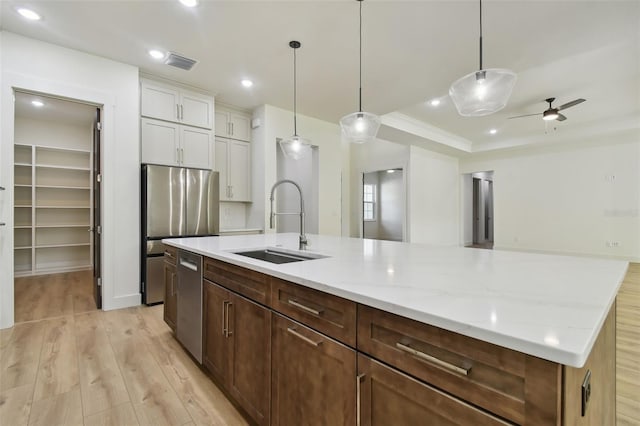 kitchen featuring a kitchen island with sink, pendant lighting, light hardwood / wood-style flooring, sink, and white cabinetry