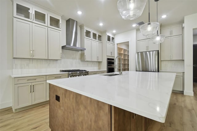 kitchen featuring appliances with stainless steel finishes, light wood-type flooring, wall chimney range hood, and a spacious island