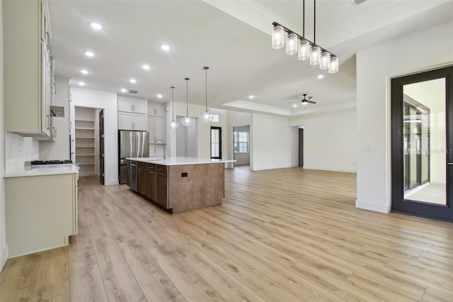 kitchen with an island with sink, ceiling fan, sink, light hardwood / wood-style floors, and decorative light fixtures