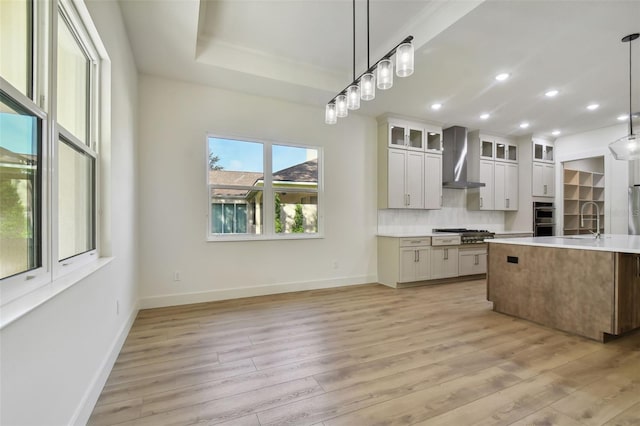 kitchen with wall chimney exhaust hood, light hardwood / wood-style flooring, decorative light fixtures, sink, and white cabinetry