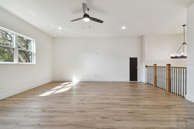 spare room with ceiling fan with notable chandelier and light hardwood / wood-style flooring