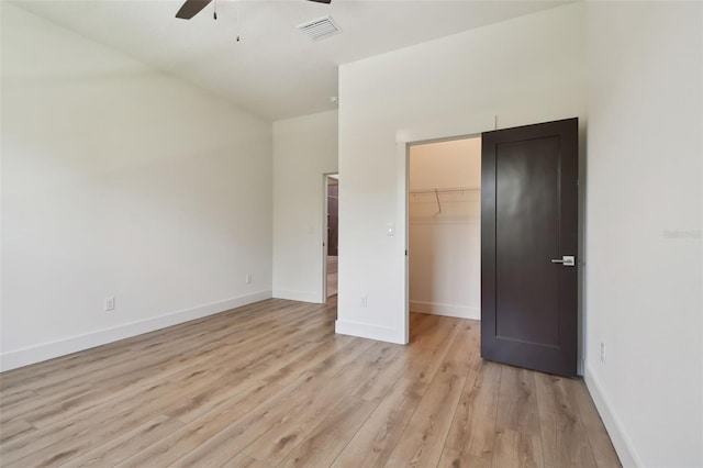 unfurnished bedroom featuring a spacious closet, a closet, light wood-type flooring, and ceiling fan