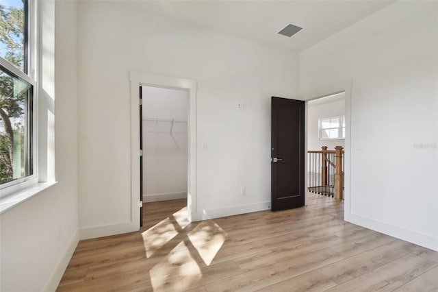 unfurnished bedroom with light wood-type flooring, multiple windows, a closet, and a walk in closet