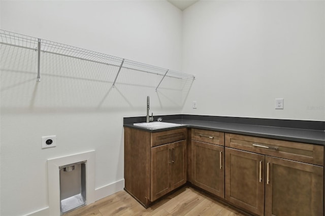 laundry area with electric dryer hookup, cabinets, sink, and light hardwood / wood-style flooring