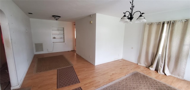 unfurnished dining area featuring built in shelves, light wood-type flooring, and a chandelier