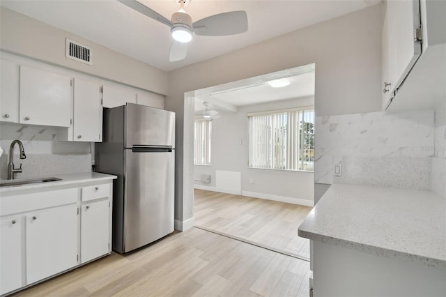 kitchen featuring sink, light hardwood / wood-style floors, stainless steel refrigerator, tasteful backsplash, and white cabinetry