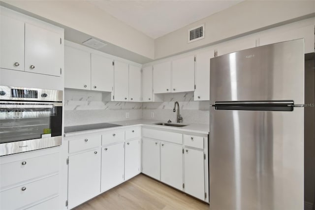 kitchen with white cabinetry, backsplash, light hardwood / wood-style floors, sink, and stainless steel appliances