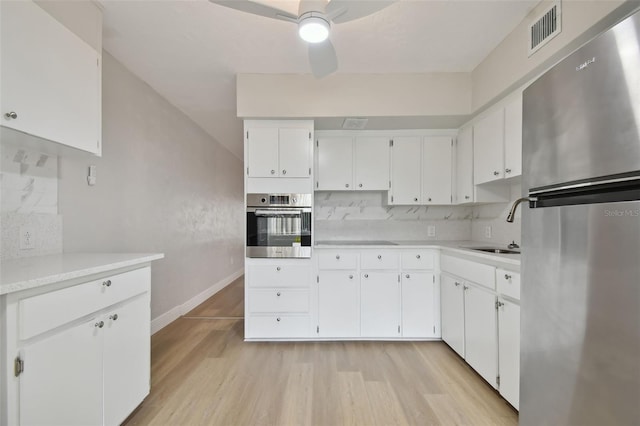 kitchen featuring ceiling fan, light hardwood / wood-style flooring, stainless steel appliances, tasteful backsplash, and white cabinetry