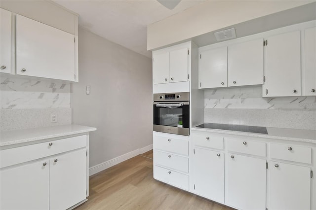 kitchen featuring oven, white cabinets, light hardwood / wood-style floors, tasteful backsplash, and black electric stovetop