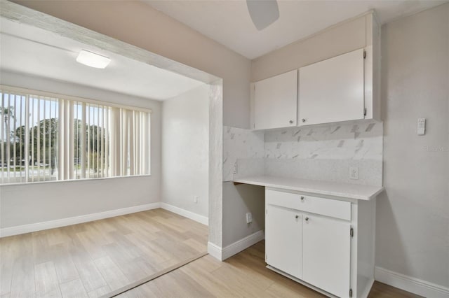 kitchen with backsplash, light hardwood / wood-style floors, white cabinetry, and built in desk