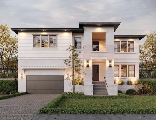 contemporary home featuring an attached garage, a balcony, decorative driveway, and brick siding