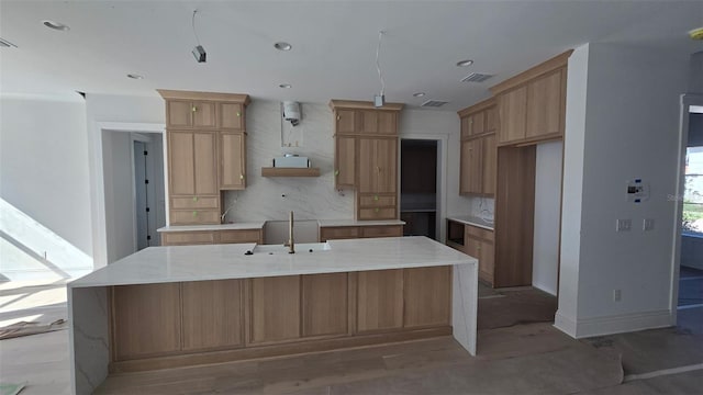 kitchen featuring baseboards, visible vents, decorative backsplash, a large island with sink, and a sink