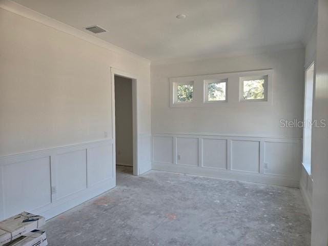 empty room featuring ornamental molding, wainscoting, visible vents, and a decorative wall