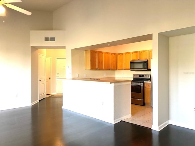 kitchen with ceiling fan, stainless steel appliances, light wood-type flooring, and a high ceiling