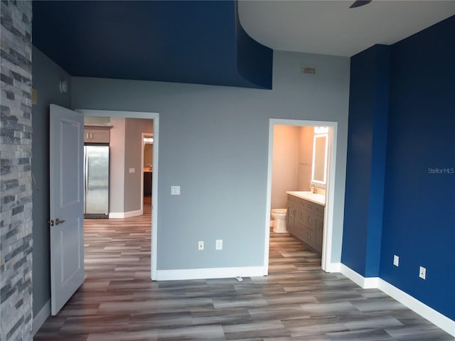 unfurnished bedroom featuring stainless steel fridge, light hardwood / wood-style floors, ensuite bath, and sink