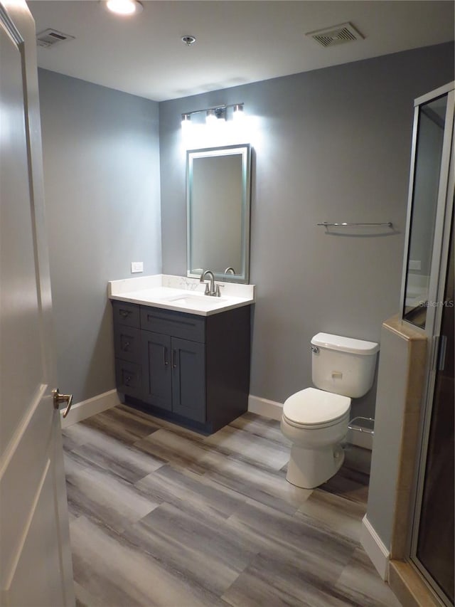 bathroom with hardwood / wood-style floors, vanity, toilet, and a shower with door