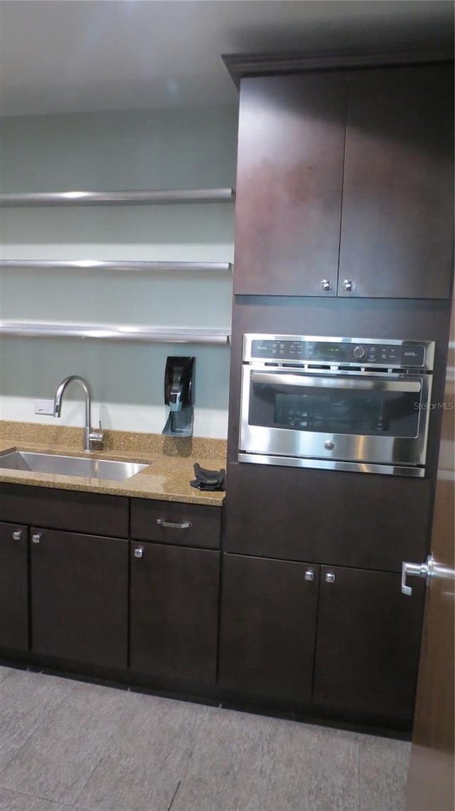 kitchen with dark brown cabinets, sink, light stone counters, and stainless steel oven