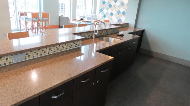 kitchen with decorative backsplash, sink, dark tile patterned floors, and light stone countertops