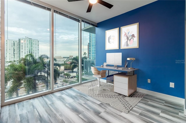 office area with plenty of natural light, ceiling fan, a wall of windows, and light hardwood / wood-style flooring