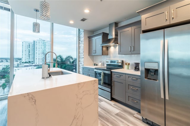 kitchen with appliances with stainless steel finishes, backsplash, sink, wall chimney range hood, and an island with sink