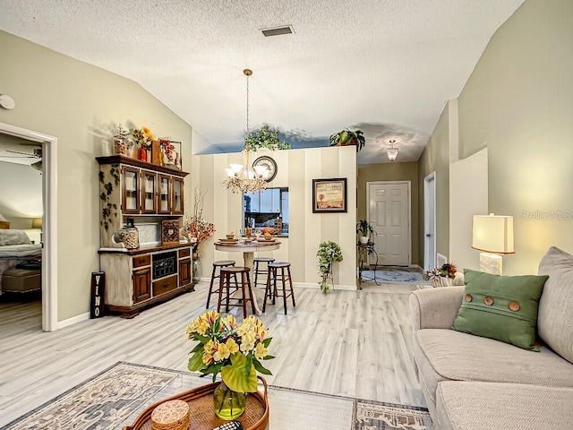 living room with lofted ceiling, a textured ceiling, ceiling fan with notable chandelier, and light hardwood / wood-style flooring