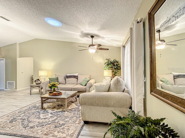 living room with lofted ceiling, light hardwood / wood-style flooring, ceiling fan, and a textured ceiling