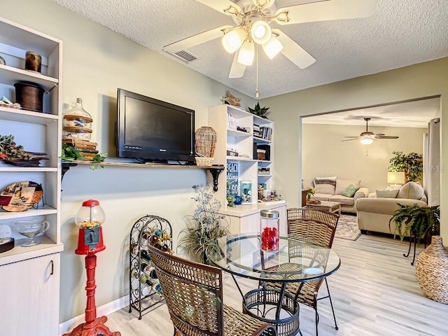 dining area with light wood-type flooring, ceiling fan, and a textured ceiling