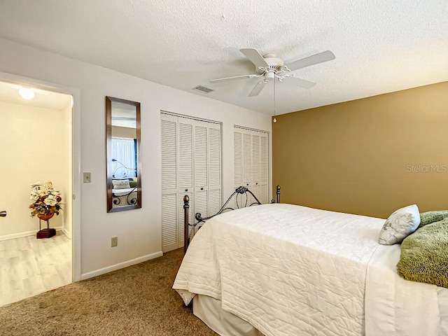 bedroom with multiple closets, a textured ceiling, dark colored carpet, and ceiling fan