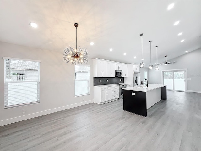 kitchen featuring vaulted ceiling, decorative light fixtures, white cabinets, stainless steel appliances, and a center island with sink