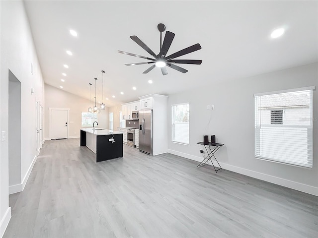 kitchen with pendant lighting, sink, white cabinets, stainless steel appliances, and a center island with sink