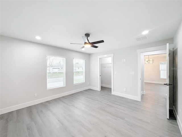 unfurnished bedroom with ceiling fan, a spacious closet, a closet, and light hardwood / wood-style flooring