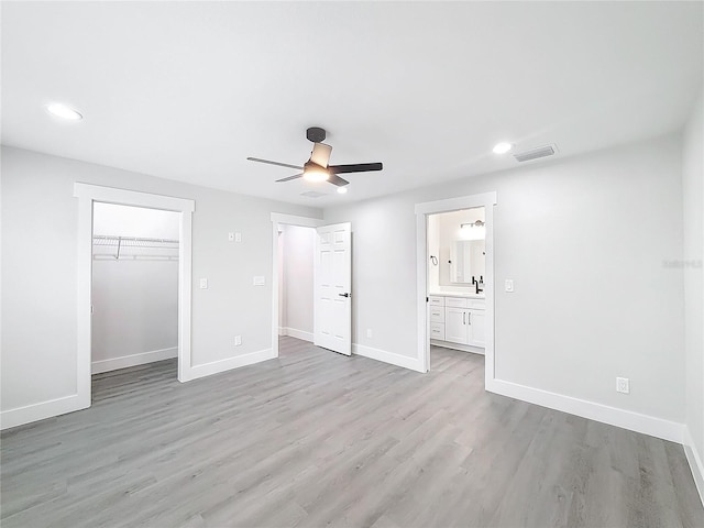 unfurnished bedroom featuring sink, ceiling fan, ensuite bathroom, light hardwood / wood-style floors, and a closet