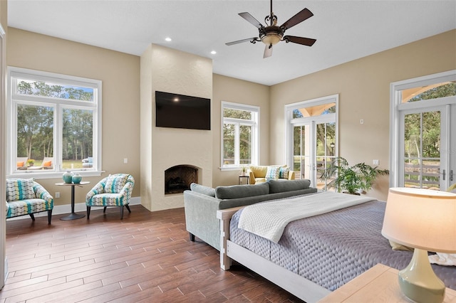 bedroom with access to outside, a large fireplace, dark hardwood / wood-style floors, and ceiling fan