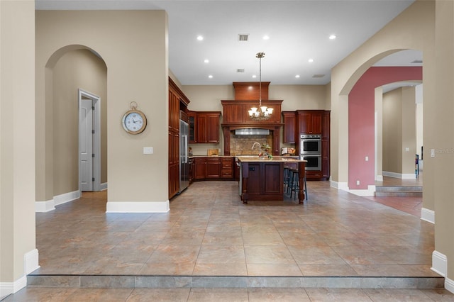 kitchen featuring decorative backsplash, appliances with stainless steel finishes, a kitchen breakfast bar, pendant lighting, and an island with sink