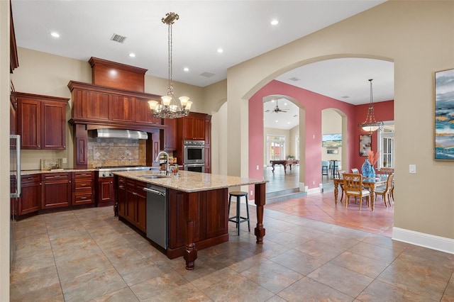 kitchen with light stone counters, sink, pendant lighting, and a center island with sink