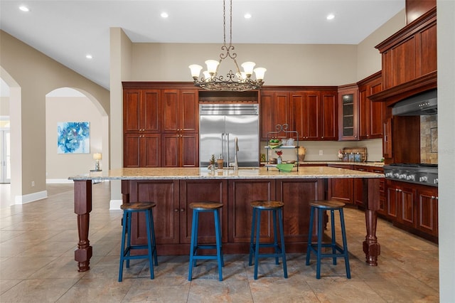 kitchen with light stone countertops, appliances with stainless steel finishes, a breakfast bar, a kitchen island with sink, and an inviting chandelier