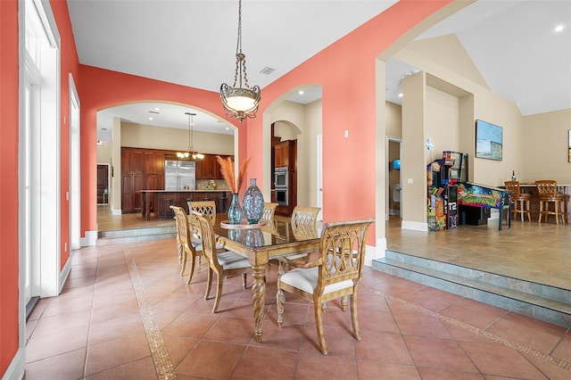 tiled dining room with high vaulted ceiling, a healthy amount of sunlight, and a notable chandelier