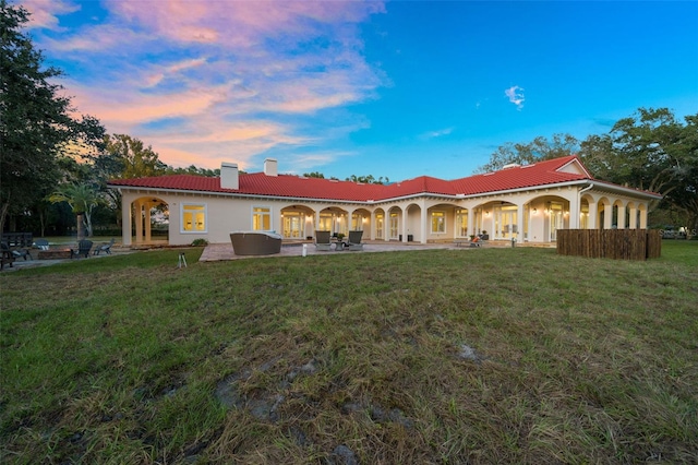 back house at dusk with outdoor lounge area, a patio area, and a lawn