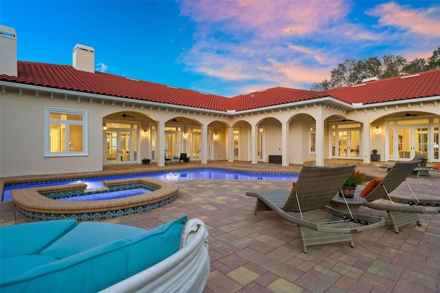 back house at dusk featuring a swimming pool with hot tub, ceiling fan, french doors, and a patio