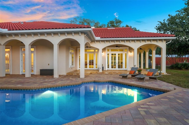 back house at dusk with french doors, ceiling fan, and a patio area