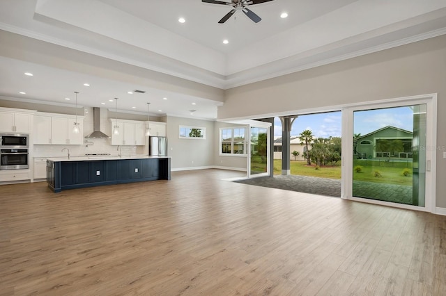 unfurnished living room with crown molding, sink, ceiling fan, and light wood-type flooring