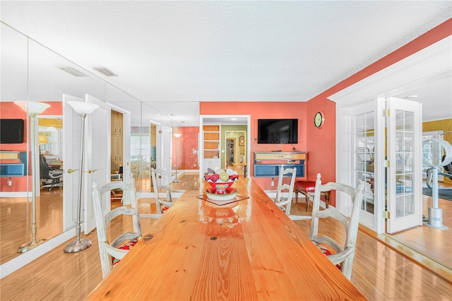 dining area featuring french doors, light hardwood / wood-style floors, and a textured ceiling