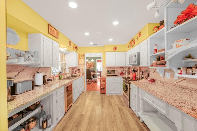 kitchen featuring tasteful backsplash, appliances with stainless steel finishes, white cabinets, light wood-type flooring, and sink