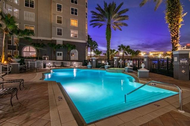 pool at dusk featuring pool water feature and a patio area