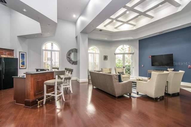 living room featuring a high ceiling, plenty of natural light, dark wood-type flooring, and coffered ceiling