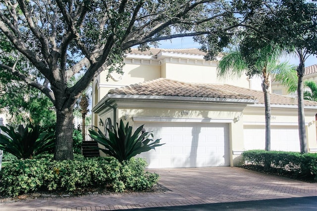 view of front of property featuring a tiled roof, decorative driveway, an attached garage, and stucco siding