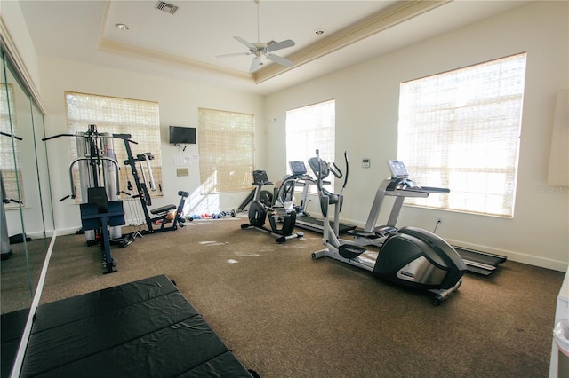 gym with ceiling fan, a healthy amount of sunlight, and a tray ceiling