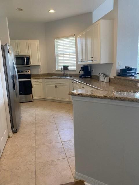 kitchen featuring sink, kitchen peninsula, dark stone countertops, light tile patterned floors, and appliances with stainless steel finishes