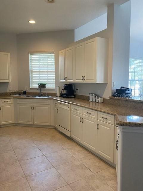 kitchen featuring white dishwasher, white cabinetry, light tile patterned floors, and stone counters