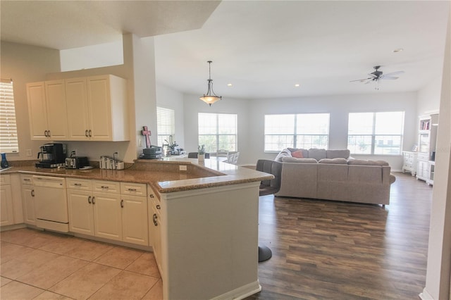 kitchen featuring kitchen peninsula, pendant lighting, white dishwasher, and dark stone counters